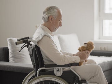 Hombre mayor en silla de ruedas sujetando un peluche