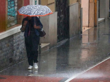 Una mujer bajo una paraguas camina por intensa lluvia