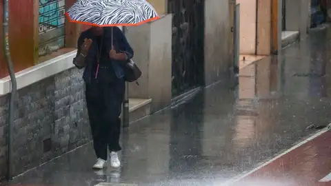 Una mujer bajo una paraguas camina por intensa lluvia Una mujer bajo una paraguas camina por intensa lluvia