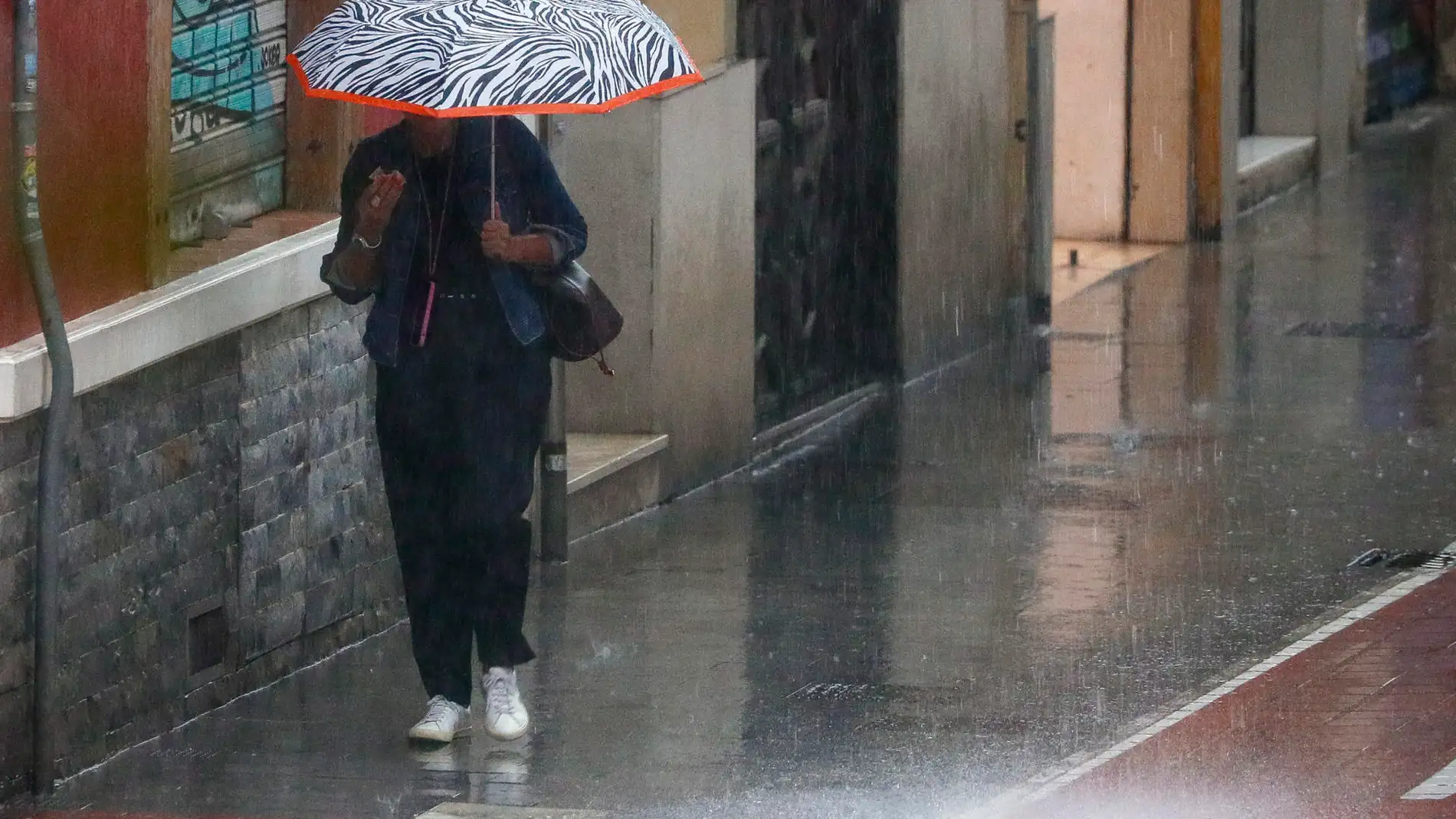 Una mujer bajo una paraguas camina por intensa lluvia