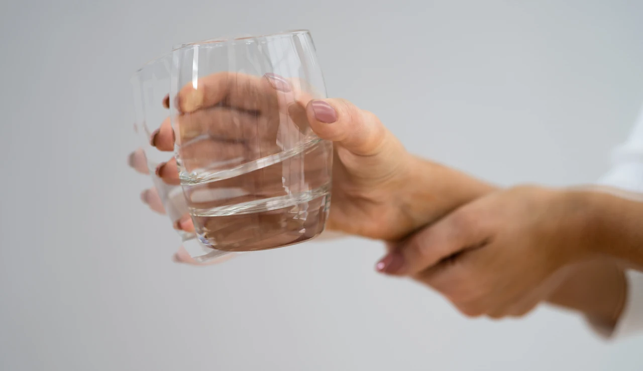 Mano de mujer sujetando un vaso de agua con temblores como con la enfermedad de Parkinson