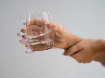 Mano de mujer sujetando un vaso de agua con temblores como con la enfermedad de Parkinson