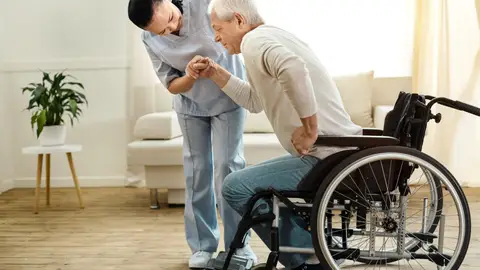 Hombre mayor en silla de ruedas tratando de levantarse con ayuda Hombre mayor en silla de ruedas tratando de levantarse con ayuda