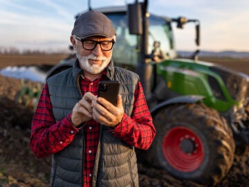 Hombre mayor con el teléfono móvil delante de un tractor
