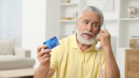 Un hombre atiende al teléfono mientras sujeta una tarjeta de crédito Un hombre atiende al teléfono mientras sujeta una tarjeta de crédito