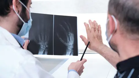 Un doctor examinando las articulaciones de un hombre a través de una radiografía Un doctor examinando las articulaciones de un hombre a través de una radiografía
