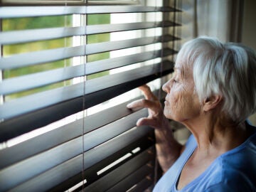 Mujer mirando a trav&eacute;s de una persiana
