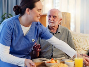 Persona cuidadora llevando la comida a un hombre mayor