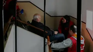 Asistencia de Cruz Roja con silla oruga para ayudar a un hombre con movilidad reducida a salir de su vivienda, en un edificio afectado por la dana.