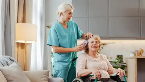 Cuidadora cepillando el pelo a una mujer mayor en silla de ruedas Cuidadora cepillando el pelo a una mujer mayor en silla de ruedas