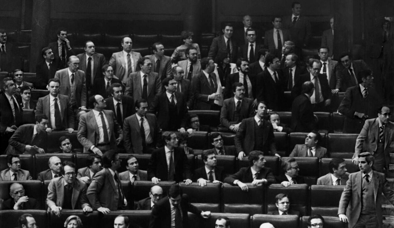 Los diputados se levantan de sus esca&ntilde;os y miran hacia la puerta por la que el teniente coronel de la Guardia Civil Antonio Tejero, pistola en mano