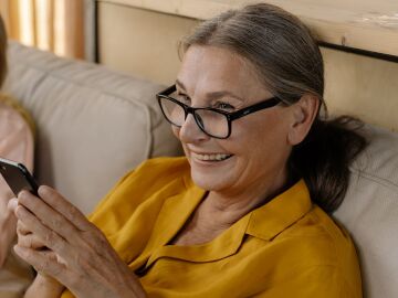 Mujer mayor y ni&ntilde;a peque&ntilde;a disfrutando tiempo juntas, conect&aacute;ndose a trav&eacute;s de un tel&eacute;fono inteligente en interiores