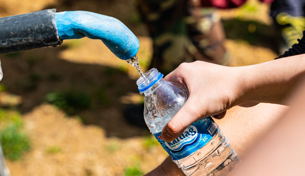 Personas llenando botellas de agua de una fuente exterior 