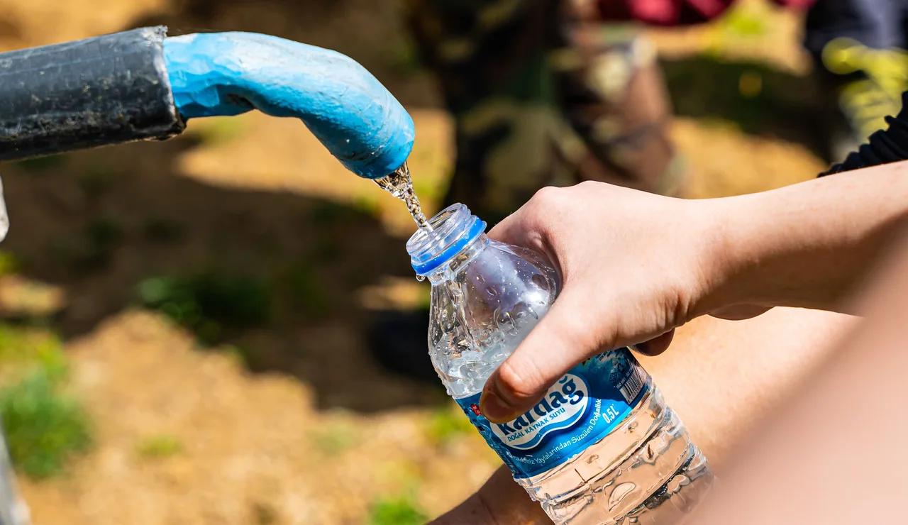 Personas llenando botellas de agua de una fuente exterior
