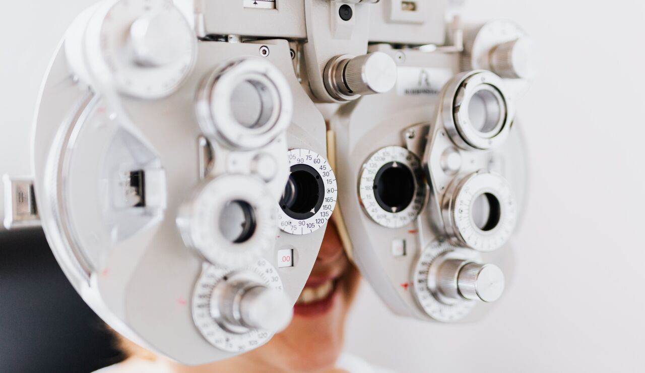 Primer plano de una mujer someti&eacute;ndose a un examen ocular usando un for&oacute;metro para probar la visi&oacute;n