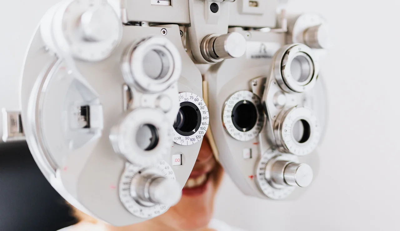 Primer plano de una mujer sometiéndose a un examen ocular usando un forómetro para probar la visión