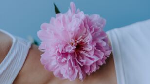 Una toma en primer plano que destaca una vibrante peon&iacute;a rosa colocada sobre piel desnuda, irradiando elegancia y simplicidad.