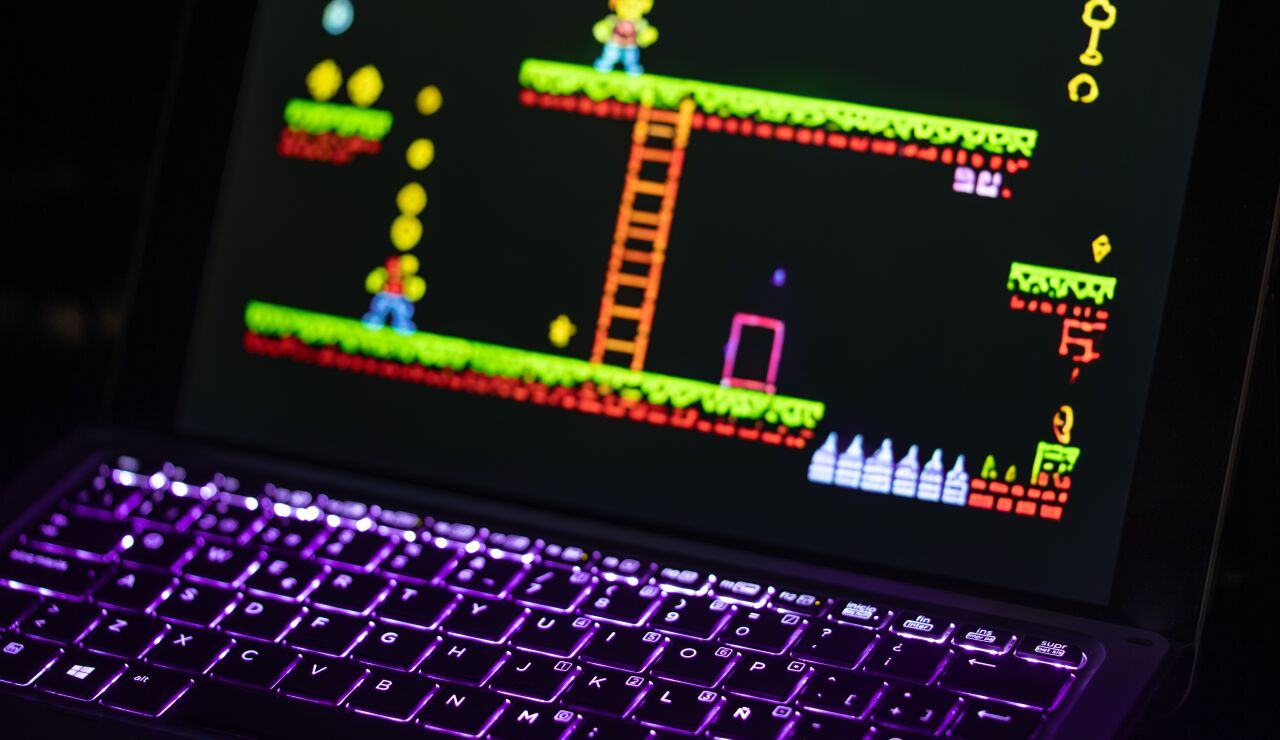 Primer plano de un port&aacute;til que muestra un videojuego retro con un teclado iluminado con luces de ne&oacute;n, capturando la experiencia nost&aacute;lgica del juego