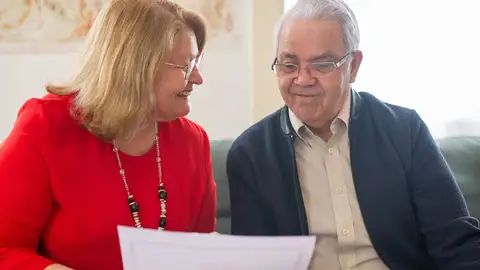 Pareja de ancianos consultando opciones de pensiones, sonriendo en un sofá, discutiendo documentos. Pareja de ancianos consultando opciones de pensiones, sonriendo en un sofá, discutiendo documentos.