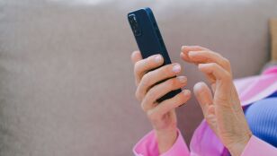 Un adulto mayor con chaqueta rosa usando un smartphone mientras se relaja en un sof&aacute; en interiores