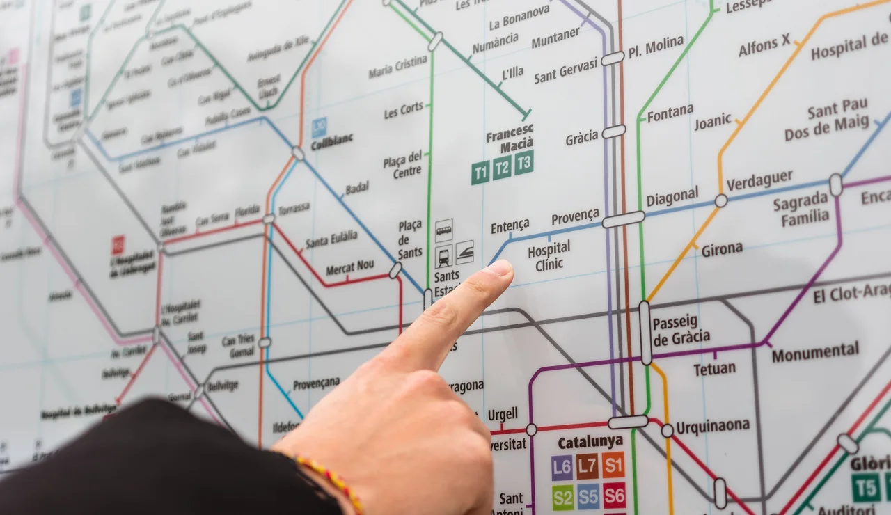 Una persona señala una estación en el detallado mapa del metro de Barcelona en interiores.