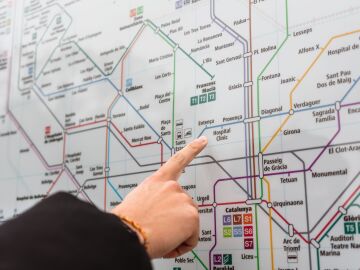 Una persona se&ntilde;ala una estaci&oacute;n en el detallado mapa del metro de Barcelona en interiores.