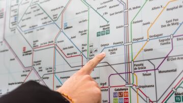 Una persona se&ntilde;ala una estaci&oacute;n en el detallado mapa del metro de Barcelona en interiores.