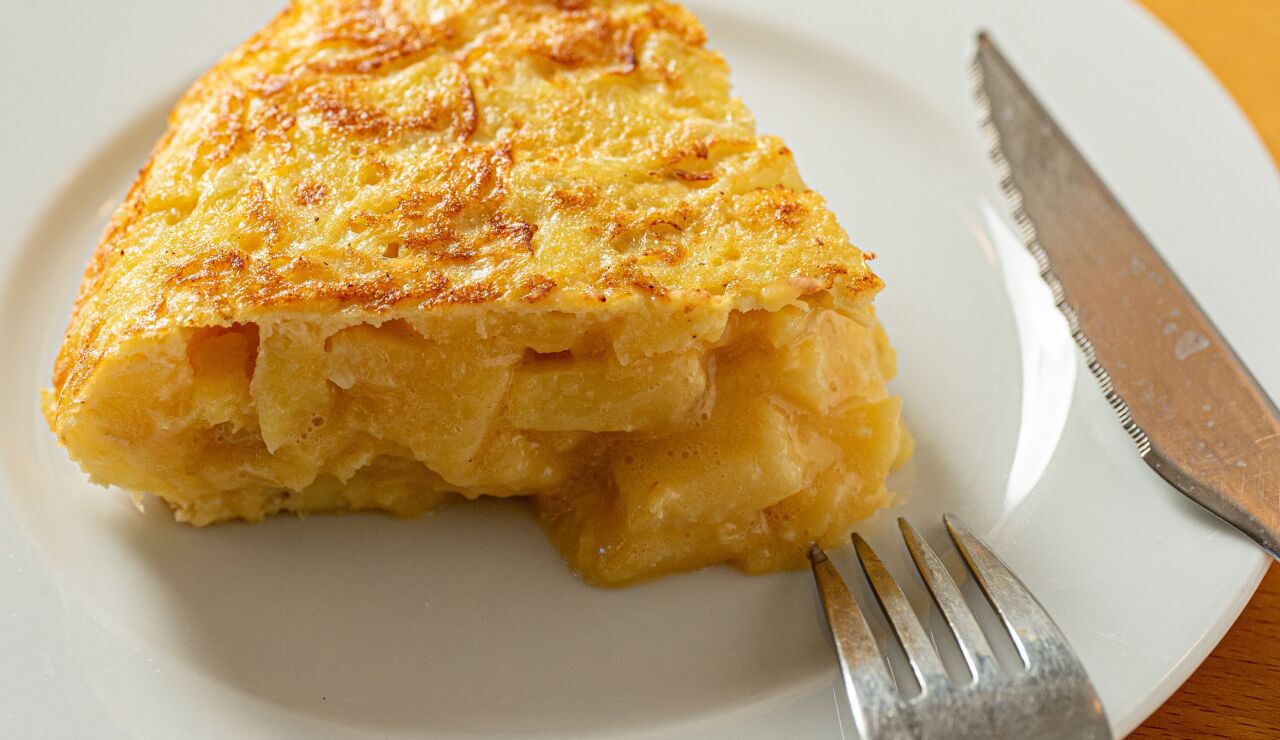 Una deliciosa porci&oacute;n de tortilla espa&ntilde;ola con un tenedor y un cuchillo en un plato blanco
