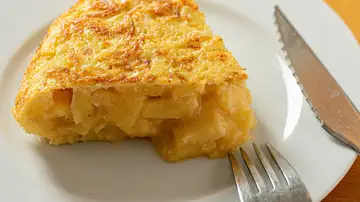 Una deliciosa porción de tortilla española con un tenedor y un cuchillo en un plato blanco Una deliciosa porción de tortilla española con un tenedor y un cuchillo en un plato blanco