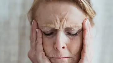 Una mujer anciana con los ojos cerrados, tocándose la cara, mostrando signos de estrés y preocupación en interiores. Una mujer anciana con los ojos cerrados, tocándose la cara, mostrando signos de estrés y preocupación en interiores.