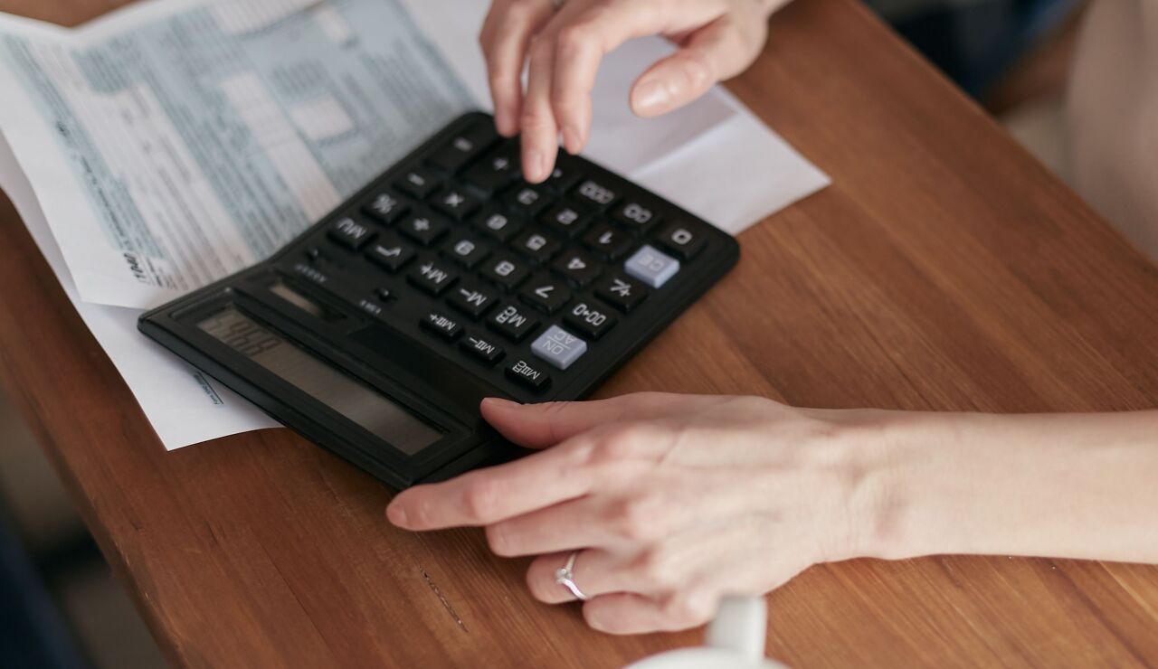 Una mujer usa una calculadora para gestionar las finanzas en casa, enfocada en la planificaci&oacute;n del presupuesto.