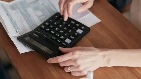 Una mujer usa una calculadora para gestionar las finanzas en casa, enfocada en la planificación del presupuesto. Una mujer usa una calculadora para gestionar las finanzas en casa, enfocada en la planificación del presupuesto.