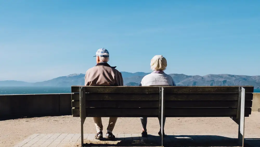 Dos ancianos sentados en un banco mirando hacia el horizonte costero