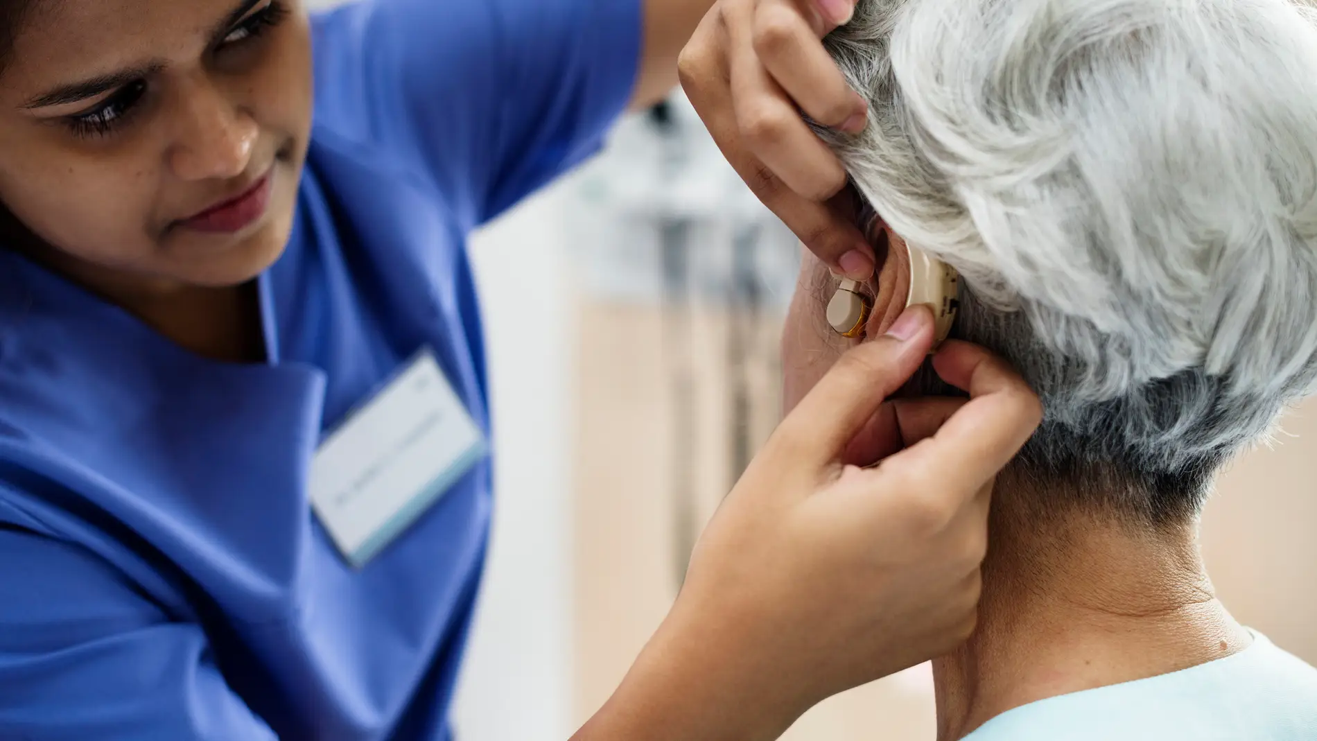 Profesional aplicando un dispositivo auditivo a una persona mayor con sordera