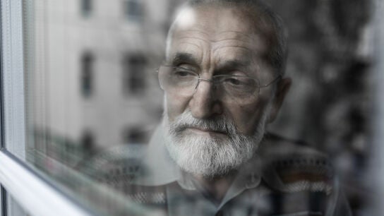 Hombre mayor mirando por la ventana triste