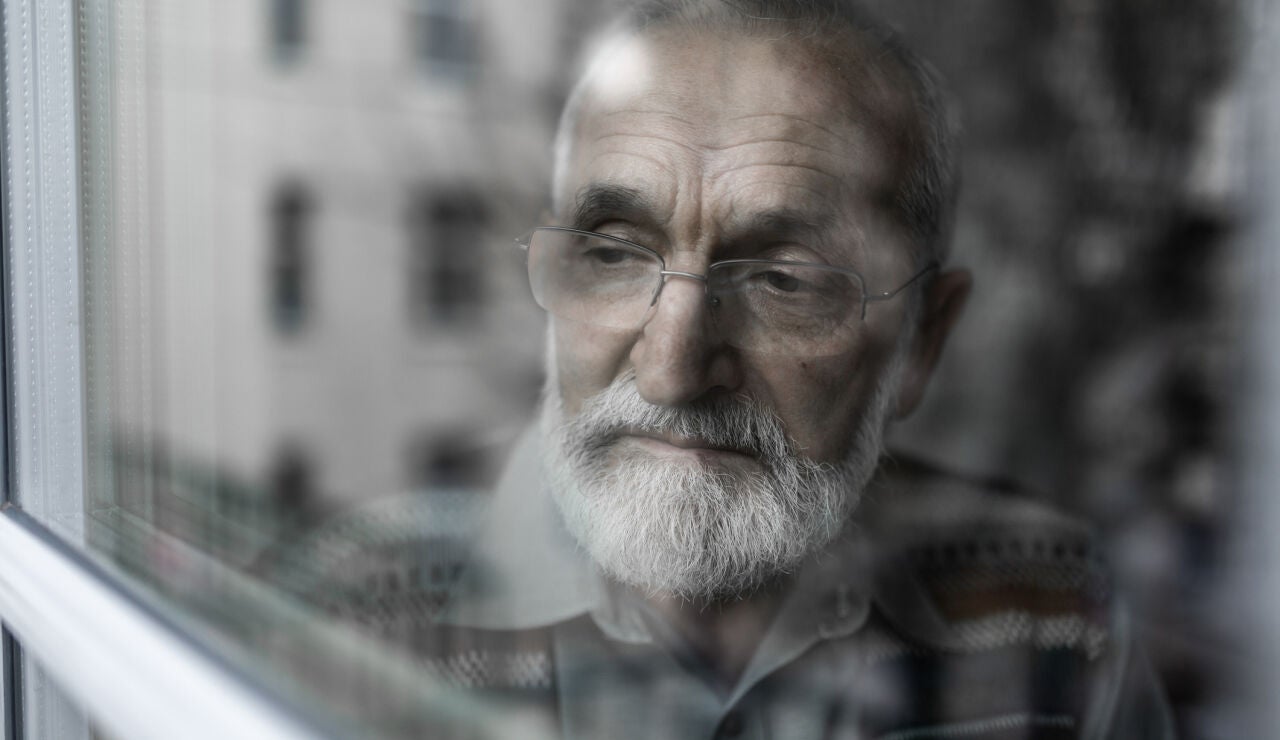 Hombre mayor mirando por la ventana triste