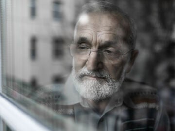 Hombre mayor mirando por la ventana triste