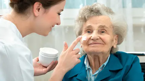 Mujer ayudando a una persona mayor a ponerse crema Mujer ayudando a una persona mayor a ponerse crema