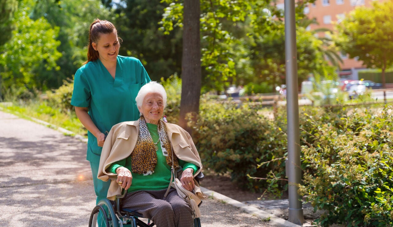 Una mujer en silla de ruedas dando un paseo junto a una cuidadora