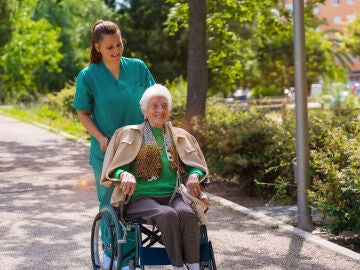 Una mujer en silla de ruedas dando un paseo junto a una cuidadora