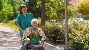 Una mujer en silla de ruedas dando un paseo junto a una cuidadora