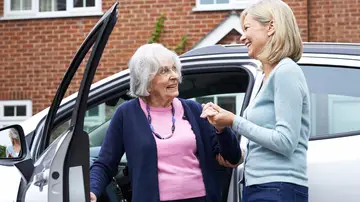 Mujer mayor saliendo de un coche ayudada por otra mujer