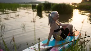Mujer mayor sentada sobre una tabla paddle surf