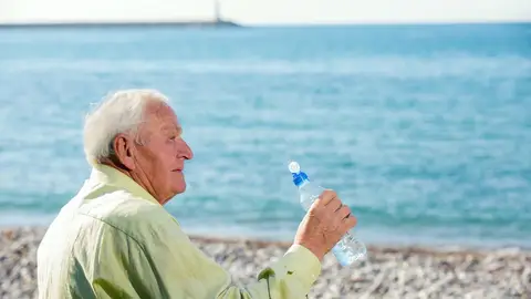 Hombre mayor frente a la playa con una botella de agua Hombre mayor frente a la playa con una botella de agua