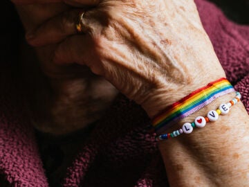 Mano de persona mayor que luce una pulsera con los colores de la bandera LGTBI