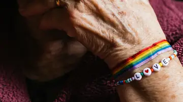 Mano de persona mayor que luce una pulsera con los colores de la bandera LGTBI