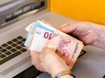 Manos de mujer mayor cogiendo dinero de un cajero
