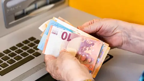 Manos de mujer mayor cogiendo dinero de un cajero Manos de mujer mayor cogiendo dinero de un cajero