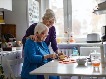 Una mujer mayor junto a un familiar ayud&aacute;ndole a cocinar