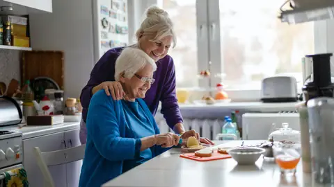Una mujer mayor junto a un familiar ayudándole a cocinar Una mujer mayor junto a un familiar ayudándole a cocinar